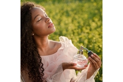 Woman with curly hair closes her eyes as she sprays perfume in the middle of a field.