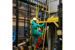 man in protective gear climbing down a ladder in a factory