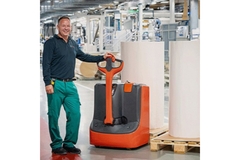 Worker standing next to two big paper rolls.