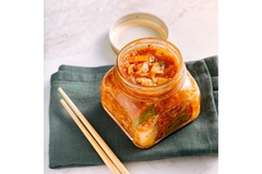 Image A jar of kimchi with two chopsticks next to it.