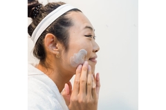 Image Side profile of woman with headband around her hair washing her face with soap.