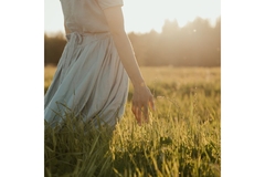 Image Back of a woman from her waist down. She wears a dress and stands in the middle of tall feilds.