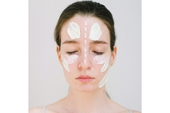 A woman with swatches of face cream on her face.