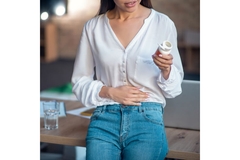 Image Woman with a hand on her stomach, holding a bottle of supplements.