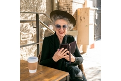 Image An women of a certain ages drinks a coffee while looking at her phone at a cafe.