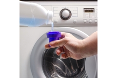 Image A hand pours liquid laundry detergent into a washing machine.
