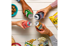 People are holding soft drinks while bags of food are placed on the table.