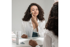 Image A woman applying her skin care looks at a mirror.