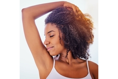 Image woman with curly hair looks to left smiling, sniffing her armpit.
