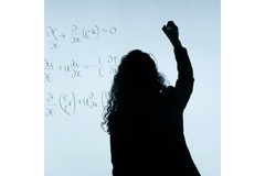 Image The shadow of a woman writing math on a white board.
