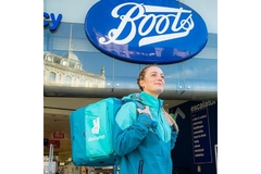 Image A female Deliveroo rider standing in front of a Boots outlet.
