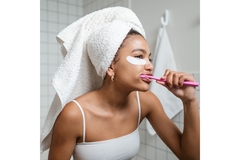 girl wearing towel on head and under eye patches brushes her teeth