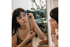 Image A woman putting on makeup while looking in the mirror.