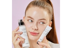 A woman holding COSRX products up on either side of her cheeks.