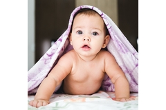 Image A cute baby lies on its belly while half covered by a purple blanket.