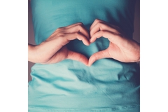 Image A woman makes the shape of heart with her hands and holds it over her stomach.