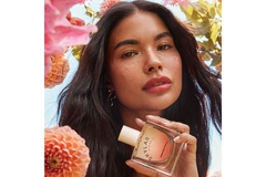 Woman surrounded by flowers holds a perfume bottle.