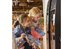two girls look into a tomra reverse vending machine with plastic bottles in hand