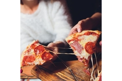 People taking slices of pizza with melted cheese.