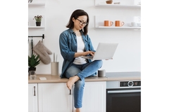 Image Woman sitting on a counter researching nutrition on her computer.