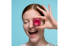 Image woman smiles with mouth open holding a cream blush container over one eye