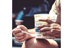 Image Man sitting outside eating yogurt from plastic cup.