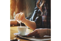 Image A woman pouring creamer over coffee.