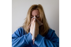 Image A woman in a blue robe blows her nose.