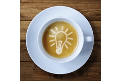 Image A white cup of coffee with lightbulb art inside it.