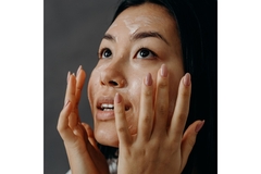 A woman touching her face while wearing moisturizer on her skin.