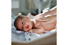 A cute baby lays on its stomach while a woman rests here hands, flat and palms down on the baby's back.