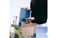 A hand putting away stuff from their desk into a box.
