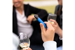 Image person holding a blue single use vape whith two other people in the background holding wine glasses