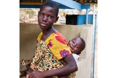 A female shea butter worker with a child on her back.