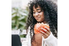 Woman on laptop eating burger.