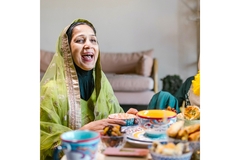 Image A Muslim woman in a green dress laughing at a food table.