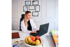 Doctor sitting behind her desk, working on her computer to look at AI screenings of patient nutritional intake.