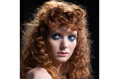A woman with 80s hair and blue eyeshadow looking to the side.