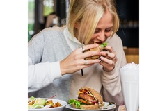 Image A woman in white sweater biting into a burger.