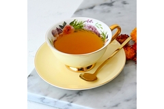 Tea in a white flowery cup with spoon on a saucer.