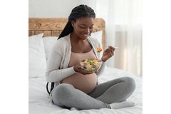 Image Pregnant woman eating a salad while sitting on bed.