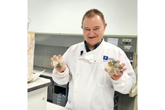 Image A male scientist in a white coat holding two petridishes with fungal strains.