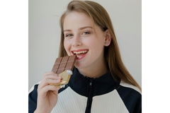Image A girl smiling and holding a bar of chocolate in her hand close to the mouth.