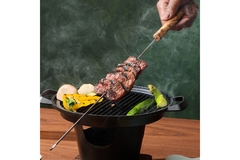 Image A hand holding cultivated meat over a grill.