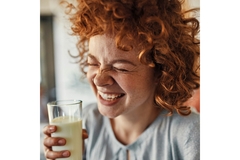 Image A curly red haired girl grinning with eyes closed with a glass of milk in her hand.
