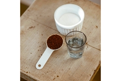 Image A spoon with instant coffee, sugar in a white ceramic bowl and water in a glass kept on a wooden table.