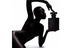 A woman in all black holding a giant perfume bottle.
