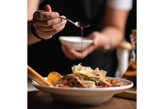 Image A hand pouring honey from a spoon into a bowl of salad.