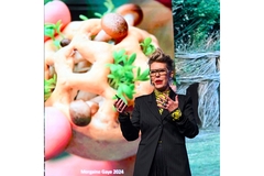 Image A woman with short hair and spectacles delivering a presentation on the stage.