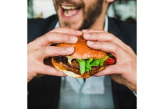 A mean eating a large burger while smiling in a resteraunt.